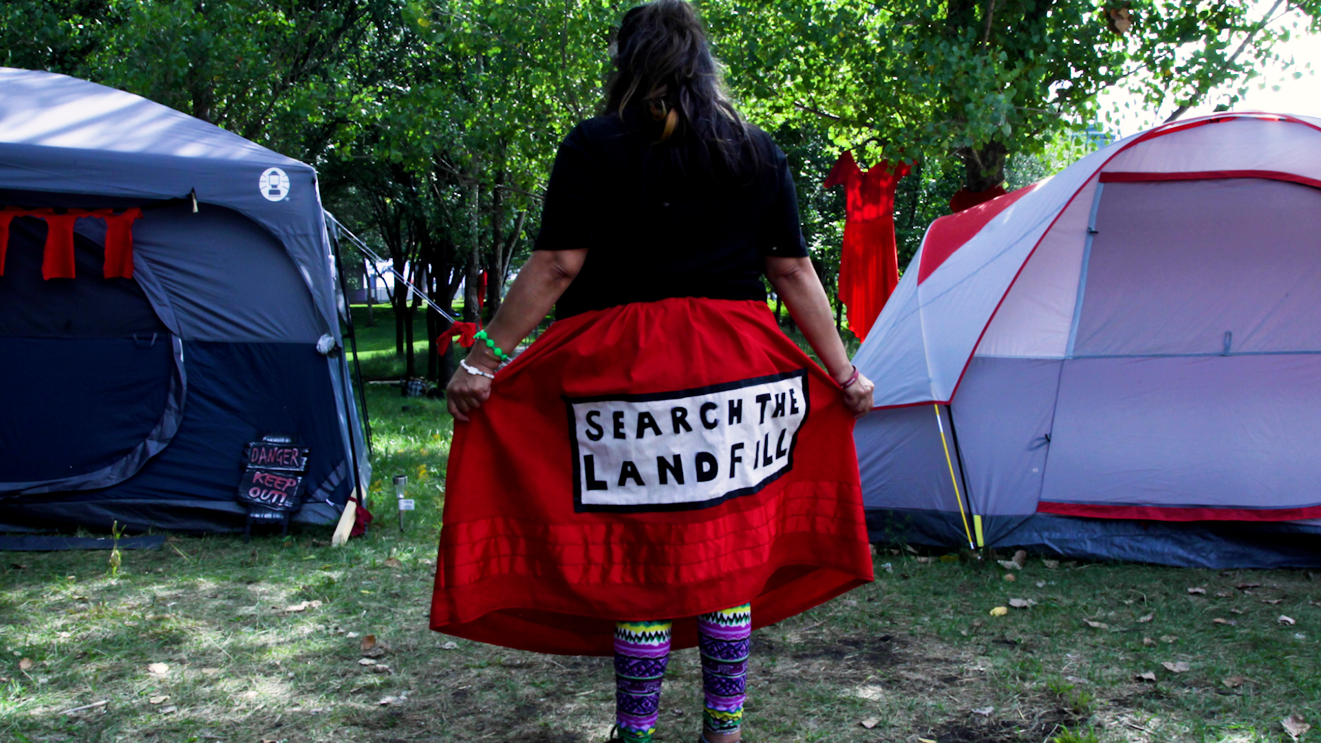 A photo of the back of a woman with the text Search the Landfill written the back of her clothes.